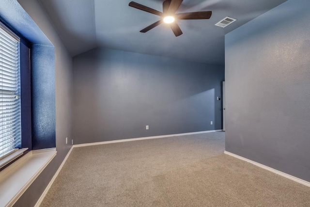 carpeted empty room with ceiling fan, vaulted ceiling, plenty of natural light, and baseboards