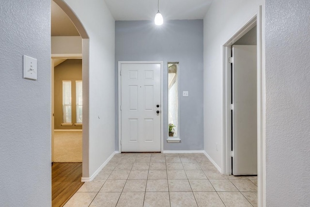 foyer with arched walkways, light tile patterned floors, and baseboards