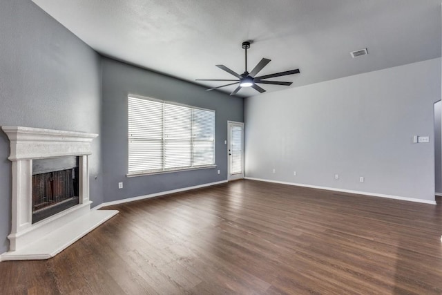 unfurnished living room featuring ceiling fan, dark wood finished floors, a fireplace with raised hearth, and baseboards