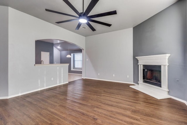 unfurnished living room featuring arched walkways, ceiling fan, wood finished floors, baseboards, and a fireplace with raised hearth