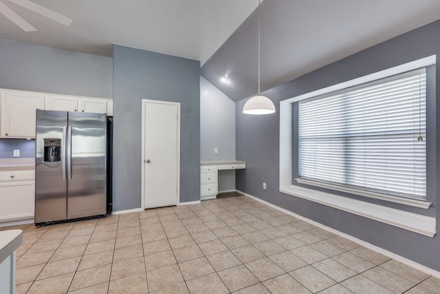 kitchen with stainless steel fridge, white cabinets, pendant lighting, vaulted ceiling, and baseboards