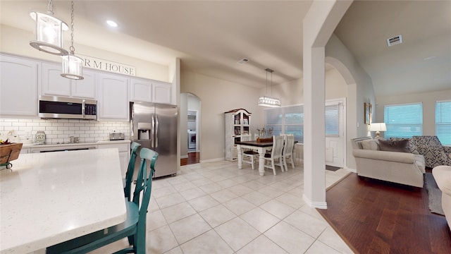 kitchen with appliances with stainless steel finishes, arched walkways, white cabinetry, backsplash, and light tile patterned floors
