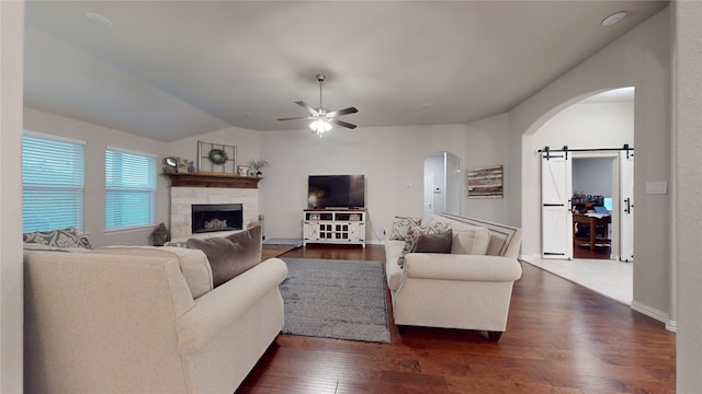 living room with arched walkways, ceiling fan, dark wood finished floors, a stone fireplace, and lofted ceiling