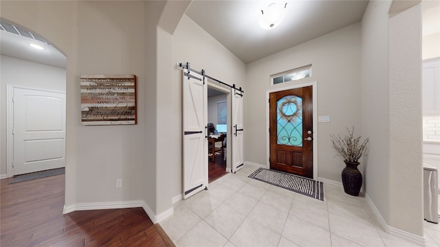 entryway with arched walkways, baseboards, a barn door, and light wood finished floors