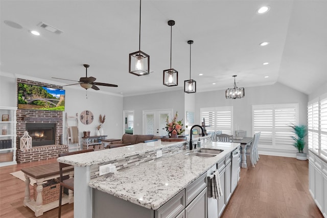 kitchen with a sink, open floor plan, a ceiling fan, a brick fireplace, and light wood-style floors