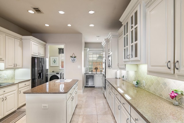 2048 Remington Ln, Frisco, TX 75033 - kitchen with washing machine and dryer, stainless steel appliances, wine cooler, a center island, and light stone counters