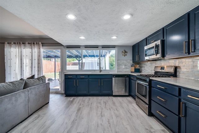 1301 Windy Meadow Dr, Plano, TX 75023 - kitchen featuring stainless steel appliances, a sink, blue cabinets, a textured ceiling, and decorative backsplash