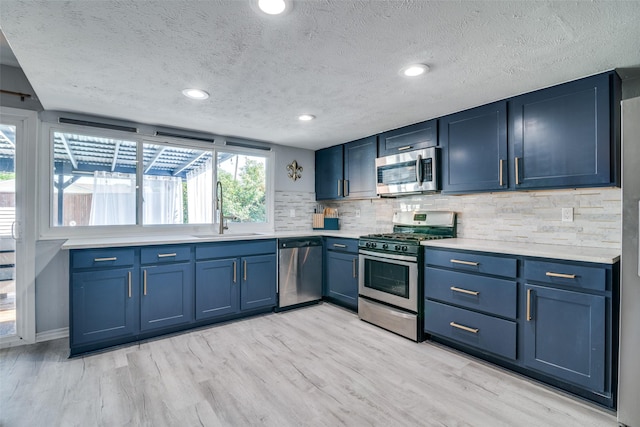 1301 Windy Meadow Dr, Plano, TX 75023 - kitchen featuring stainless steel appliances, a sink, blue cabinets, backsplash, and light wood-style flooring