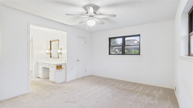 unfurnished bedroom featuring light carpet, a textured ceiling, baseboards, ensuite bath, and ceiling fan