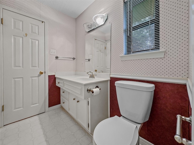 half bathroom with toilet, vanity, tile patterned floors, wallpapered walls, and baseboards