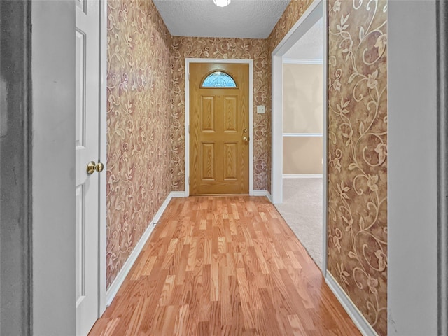 entryway with wallpapered walls, a textured ceiling, light wood-style flooring, and baseboards