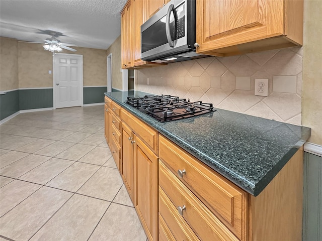 kitchen featuring stainless steel microwave, black gas stovetop, a ceiling fan, tasteful backsplash, and light tile patterned flooring