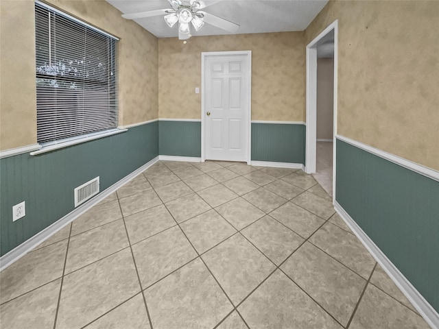 tiled empty room featuring a wainscoted wall and ceiling fan