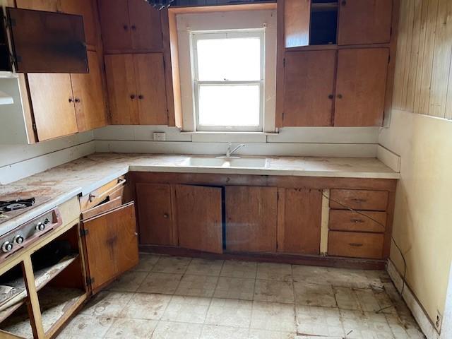 kitchen with light countertops, a sink, exhaust hood, and brown cabinets