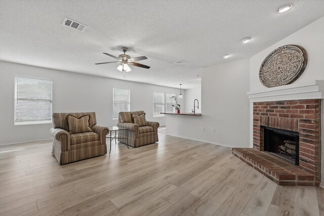 3110 Legend Dr, Mckinney, TX 75070 - living room featuring light wood-style floors, ceiling fan, a textured ceiling, a fireplace, and baseboards