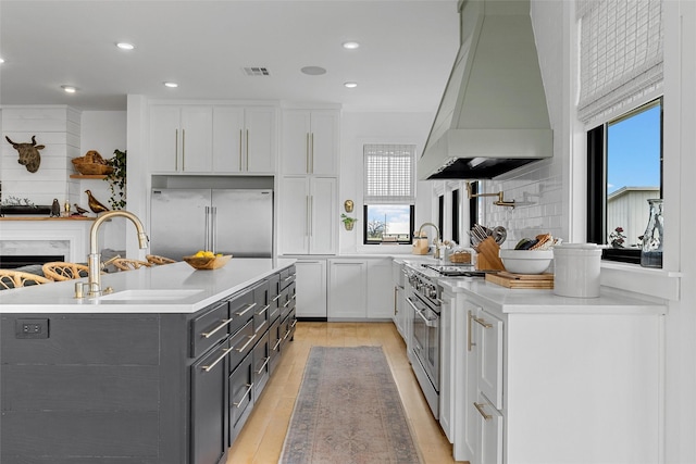1197 Prairie Chapel Rd, Crawford, TX 76638 - kitchen with custom exhaust hood, a sink, high quality appliances, white cabinets, and light wood-style floors