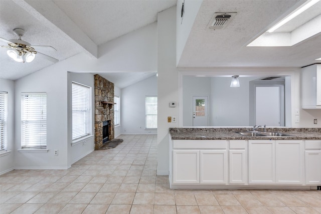 kitchen with a sink, vaulted ceiling, a fireplace, light tile patterned floors, and white cabinets