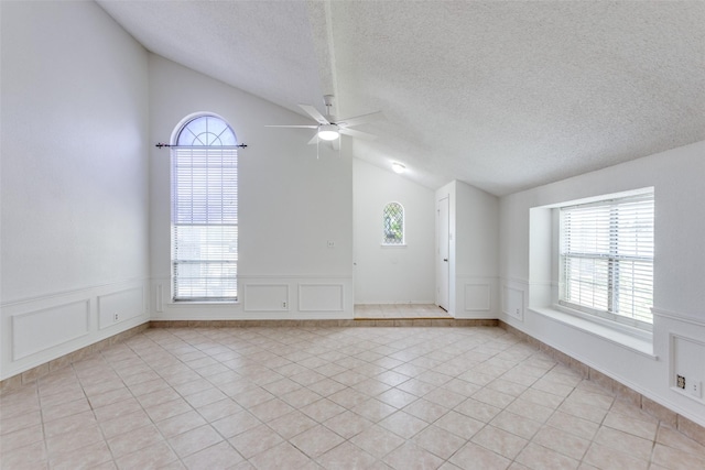 empty room with vaulted ceiling, a decorative wall, healthy amount of natural light, ceiling fan, and light tile patterned flooring