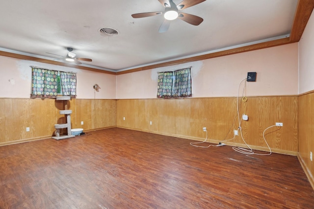 spare room with ceiling fan, a wainscoted wall, wood finished floors, and wood walls