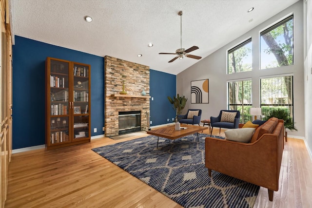 living room featuring a textured ceiling, a stone fireplace, wood finished floors, ceiling fan, and high vaulted ceiling