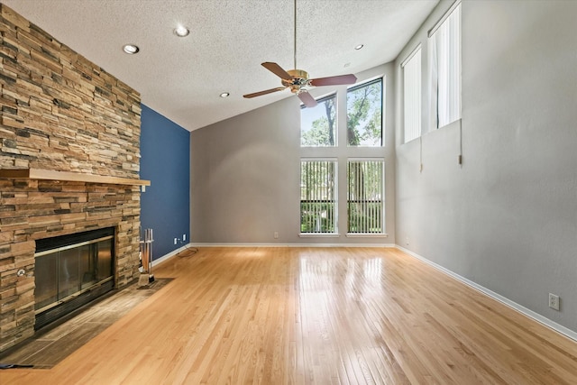 unfurnished living room with a textured ceiling, a ceiling fan, light wood-type flooring, a stone fireplace, and baseboards