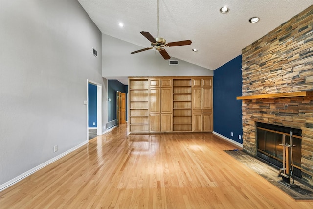 unfurnished living room featuring a ceiling fan, a stone fireplace, a textured ceiling, light wood-style floors, and baseboards