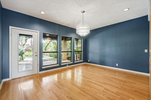 unfurnished room featuring a chandelier, plenty of natural light, wood finished floors, a textured ceiling, and baseboards