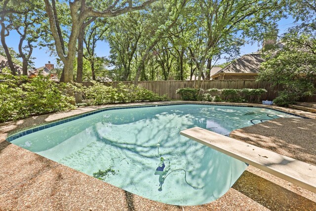 view of swimming pool with a diving board and a fenced backyard