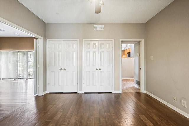 unfurnished bedroom with multiple closets, dark wood-style floors, baseboards, and ceiling fan