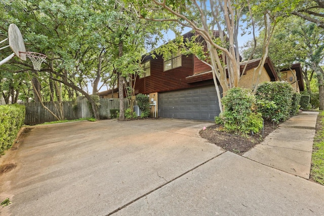 view of property exterior with fence, a garage, and concrete driveway