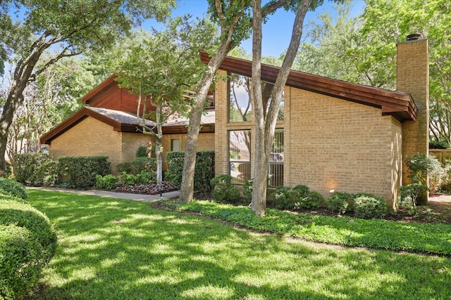 view of side of property with a chimney, brick siding, and a yard