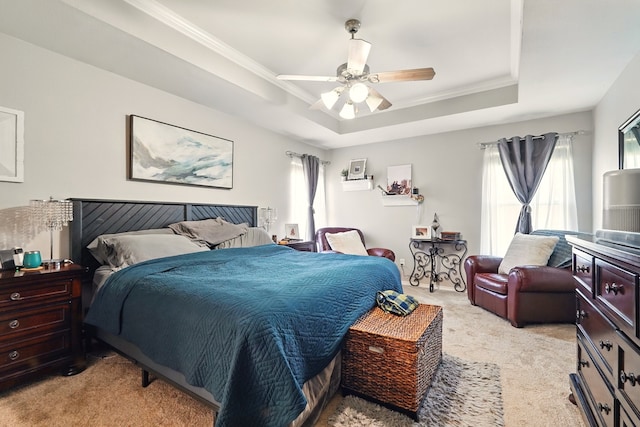 bedroom with multiple windows, light colored carpet, a raised ceiling, crown molding, and a ceiling fan