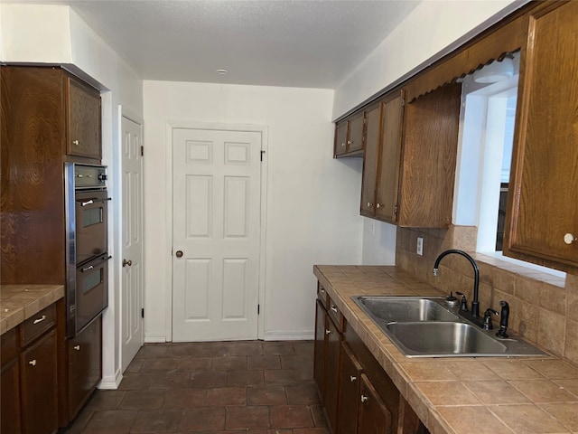 216 E Homewood Dr, Crockett, TX 75835 - kitchen with tile countertops, a sink, double wall oven, decorative backsplash, and baseboards
