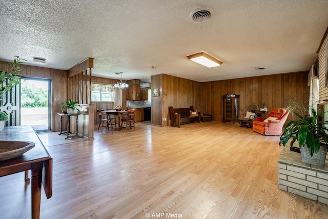 1201 New Hope Rd, Stamford, TX 79553 - living room featuring a textured ceiling, wooden walls, light wood finished floors, and a chandelier