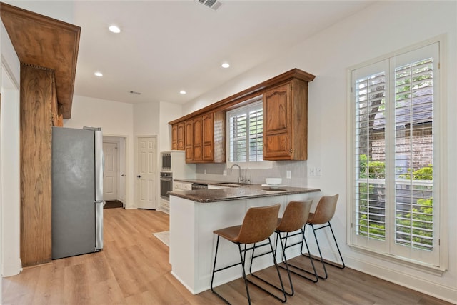 kitchen featuring stainless steel appliances, a sink, light wood-type flooring, a kitchen bar, and a peninsula