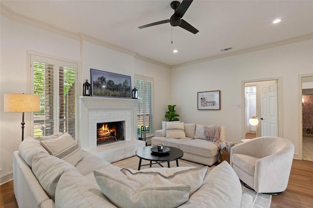 living area with crown molding, wood finished floors, ceiling fan, a brick fireplace, and recessed lighting