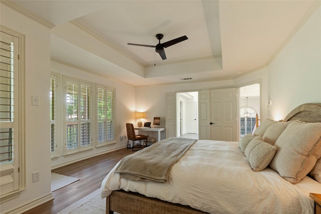 bedroom with a tray ceiling, wood finished floors, ornamental molding, a ceiling fan, and an office area