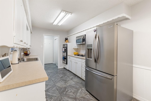 1317 Kingsbridge Dr, Garland, TX 75040 - kitchen with appliances with stainless steel finishes, a sink, white cabinets, a textured ceiling, and light countertops