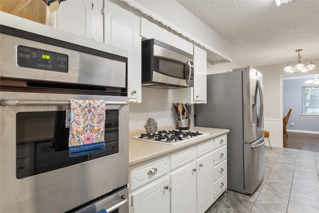 1317 Kingsbridge Dr, Garland, TX 75040 - kitchen featuring appliances with stainless steel finishes, a chandelier, a textured ceiling, light countertops, and white cabinets