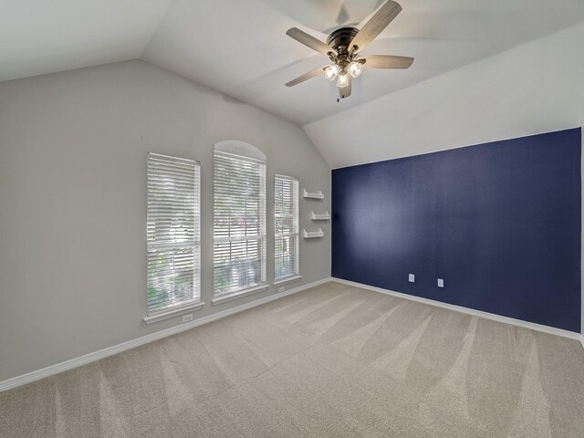 carpeted spare room with vaulted ceiling, a ceiling fan, and baseboards