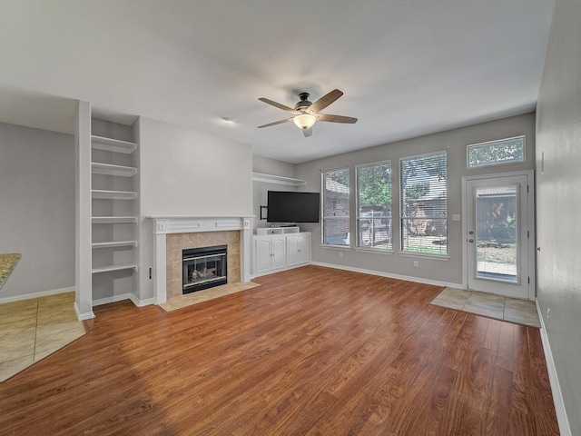 unfurnished living room with wood finished floors, ceiling fan, a tile fireplace, baseboards, and built in features