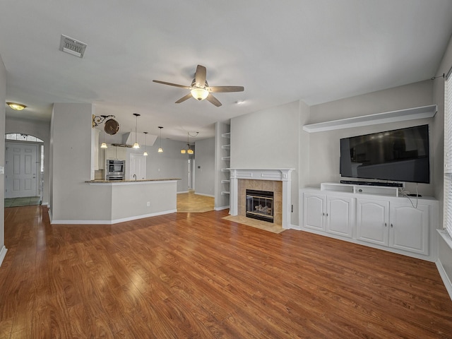 unfurnished living room with a ceiling fan, wood finished floors, baseboards, and a fireplace