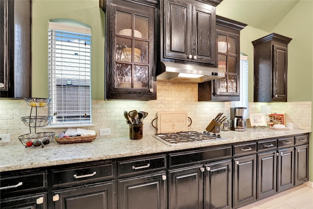 8205 Saint Clair Dr, Mckinney, TX 75071 - kitchen featuring under cabinet range hood, stainless steel gas cooktop, glass insert cabinets, backsplash, and light stone counters