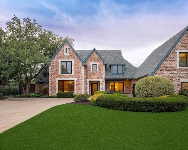 tudor home with brick siding, a front yard, driveway, and roof with shingles