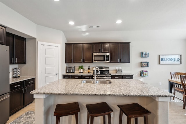 8332 Trickham Bnd, Fort Worth, TX 76131 - kitchen featuring appliances with stainless steel finishes, a breakfast bar area, a sink, dark brown cabinets, and light stone counters