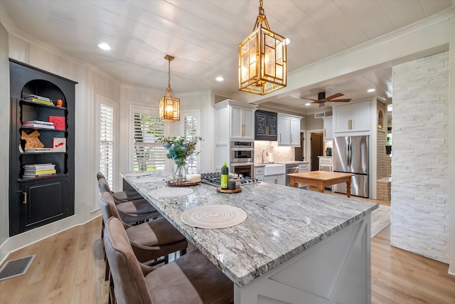 1111 Governors Dr, Corsicana, TX 75110 - kitchen featuring appliances with stainless steel finishes, ornamental molding, a ceiling fan, light wood finished floors, and white cabinetry