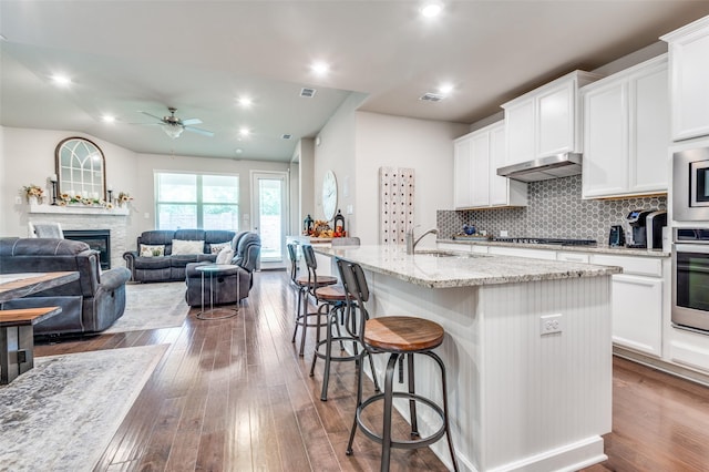 kitchen with stainless steel appliances, under cabinet range hood, ceiling fan, a sink, and dark wood-style flooring