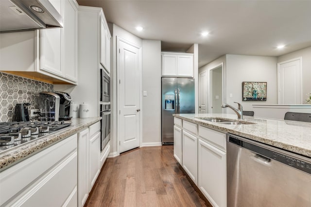 kitchen featuring stainless steel appliances, a sink, exhaust hood, white cabinets, and tasteful backsplash