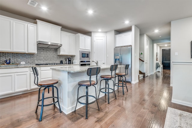 kitchen with stainless steel appliances, white cabinets, a center island with sink, light wood-style floors, and recessed lighting