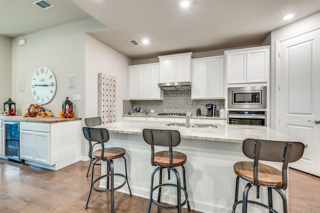 kitchen with appliances with stainless steel finishes, a sink, beverage cooler, wood finished floors, and tasteful backsplash